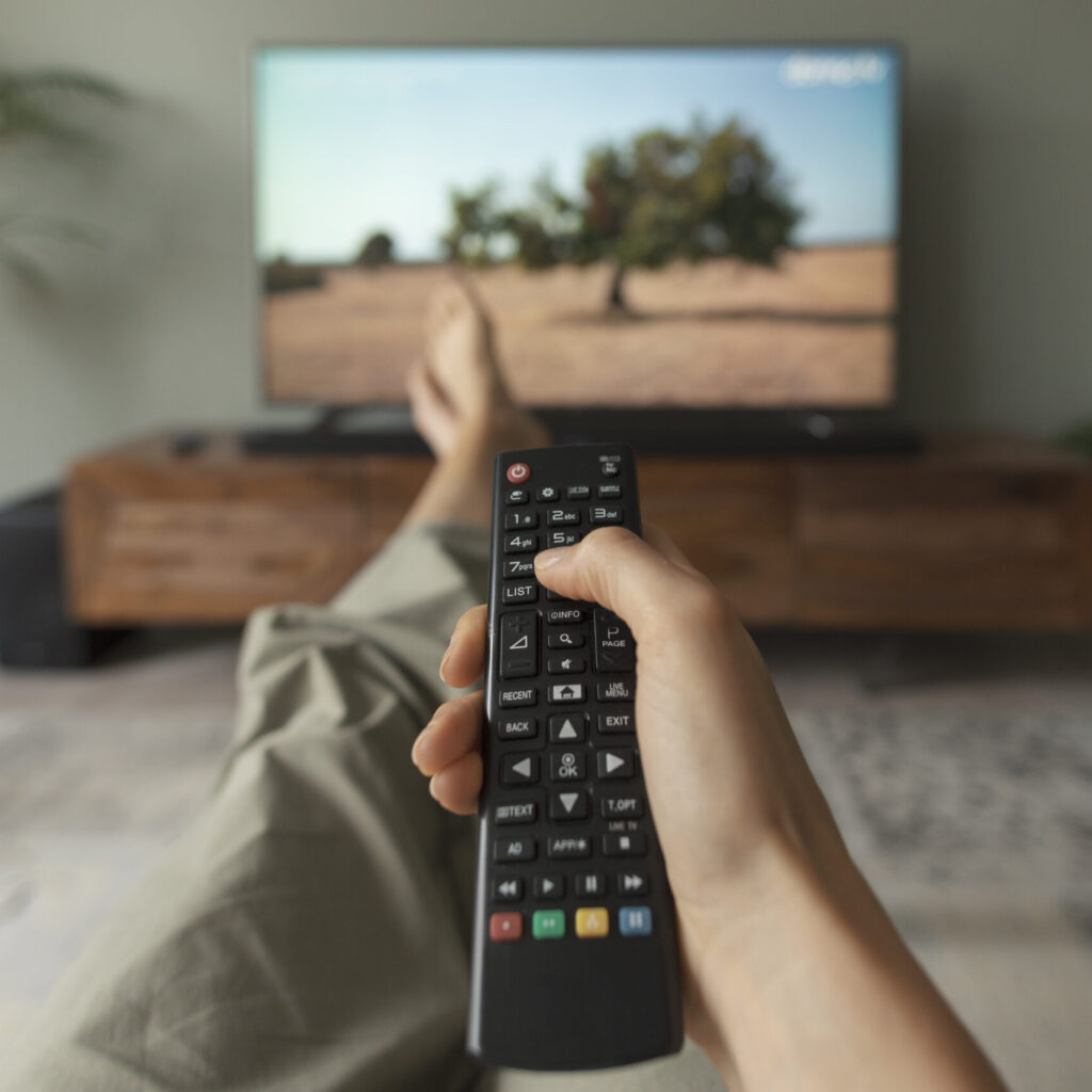 Woman watching TV at home and holding the remote control